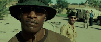 Movie still from “The Kingdom” (2007), directed by Peter Berg – A man wearing sunglasses and a hat is standing next to another man; Close Up shot, Over the shoulder angle
