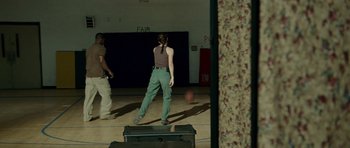 Movie still from “The Kingdom” (2007), directed by Peter Berg – A woman standing in a gym with a ball in front of her; Wide shot, Over the shoulder angle