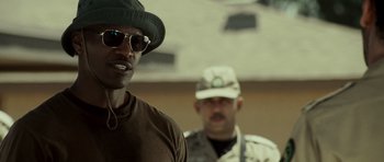 Movie still from “The Kingdom” (2007), directed by Peter Berg – A man wearing a hat and sunglasses standing next to another man in fatigues; Close Up shot, Over the shoulder angle