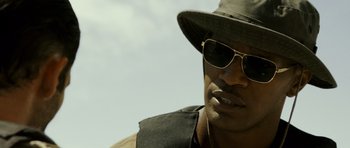 Movie still from “The Kingdom” (2007), directed by Peter Berg – A person wearing sunglasses and a hat; Close Up shot, Over the shoulder angle