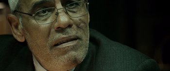 Movie still from “The Kingdom” (2007), directed by Peter Berg – An older man wearing glasses and a suit; Extreme Close Up shot, Low angle