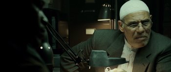 Movie still from “The Kingdom” (2007), directed by Peter Berg – A man sitting in a chair in a dark room; Close Up shot, Low angle