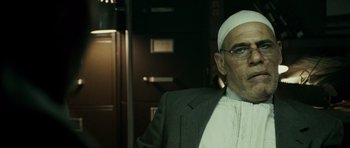 Movie still from “The Kingdom” (2007), directed by Peter Berg – An older man in a suit and white hat; Close Up shot, Low angle