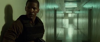 Movie still from “The Kingdom” (2007), directed by Peter Berg – A man standing in a hallway holding a gun; Close Up shot, Low angle