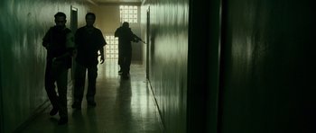 Movie still from “The Kingdom” (2007), directed by Peter Berg – Two people are walking down a hallway in a building; Wide shot, Low angle