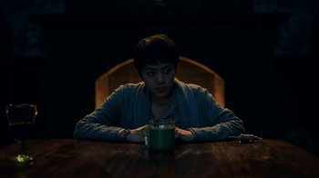 Movie still from “The Midnight Club” (2022), created by Mike Flanagan – A man sitting at a wooden table with a cup of coffee; Medium shot, High angle