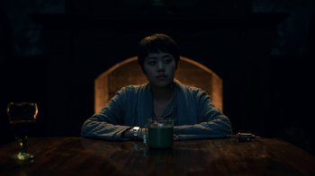 Movie still from “The Midnight Club” (2022), created by Mike Flanagan – A person sitting at a table with a cup of coffee; Medium shot, High angle