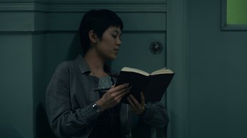 Movie still from “The Midnight Club” (2022), created by Mike Flanagan – A person standing in front of a door holding a book; Close Up shot, Over the shoulder angle