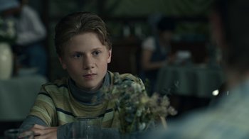 Movie still from “The Midnight Club” (2022), created by Mike Flanagan – A young boy sitting at a table holding a bouquet of flowers; Close Up shot, Over the shoulder angle