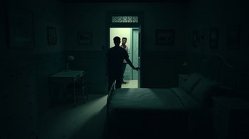 Movie still from “The Midnight Club” (2022), created by Mike Flanagan – A man and a woman standing in a dark room; Wide shot, High angle