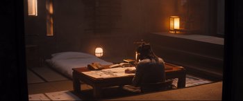 Movie still from “Bullet Train” (2022), directed by David Leitch – A person sitting at a table writing on a piece of paper; Wide shot, High angle