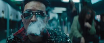 Movie still from “Bullet Train” (2022), directed by David Leitch – A man with sunglasses smoking a cigarette in a crowd; Close Up shot, Low angle