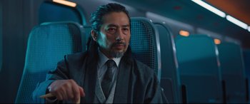 Movie still from “Bullet Train” (2022), directed by David Leitch – A man sitting on a plane wearing a suit and tie; Close Up shot, Over the shoulder angle
