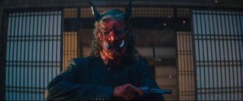 Movie still from “Bullet Train” (2022), directed by David Leitch – A person with a demon mask holding a gun; Medium shot, Low angle