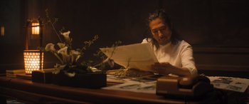 Movie still from “Bullet Train” (2022), directed by David Leitch – A man sitting at a table looking at papers; Medium shot, Low angle