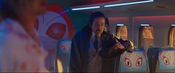 Movie still from “Bullet Train” (2022), directed by David Leitch – A man in a suit and tie standing in a room; Medium shot, Over the shoulder angle