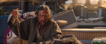 Movie still from “Bullet Train” (2022), directed by David Leitch – A man with a bloody face sitting on the ground; Medium shot, Low angle