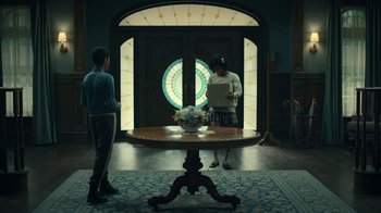 Movie still from “The Midnight Club” (2022), created by Mike Flanagan – Two men standing in front of a table in front of a stained glass window; Wide shot, Low angle