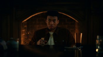Movie still from “The Midnight Club” (2022), created by Mike Flanagan – A man sitting at a table with a cigarette in his hand; Medium shot, Low angle