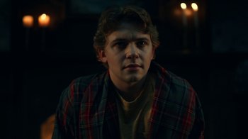 Movie still from “The Midnight Club” (2022), created by Mike Flanagan – A young man wearing a plaid shirt is looking at the camera; Close Up shot, Low angle