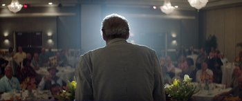Movie still from “The Mule” (2018), directed by Clint Eastwood – An older man standing in front of an audience; Medium shot, Over the shoulder angle