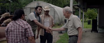 Movie still from “The Mule” (2018), directed by Clint Eastwood – A group of men standing next to each other on a dirt field; Medium shot, Over the shoulder angle