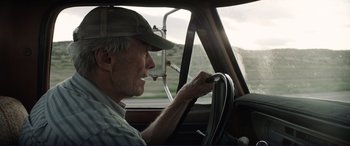 Movie still from “The Mule” (2018), directed by Clint Eastwood – An older man driving a car in the road; Close Up shot, Low angle