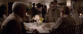 Movie still from “The Mule” (2018), directed by Clint Eastwood – A group of people standing around a table with a lamp; Medium shot, Over the shoulder angle