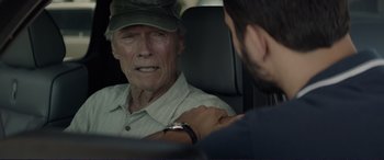 Movie still from “The Mule” (2018), directed by Clint Eastwood – An older man sitting in the back seat of a car; Close Up shot, Over the shoulder angle
