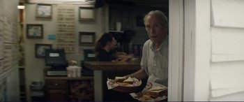 Movie still from “The Mule” (2018), directed by Clint Eastwood – An older man holding a plate of food in front of him; Medium shot, Over the shoulder angle