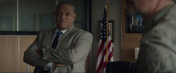 Movie still from “The Mule” (2018), directed by Clint Eastwood – A man standing in front of an american flag in an office; Medium shot, Low angle