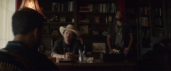 Movie still from “The Mule” (2018), directed by Clint Eastwood – A man sitting at a table in front of a book shelf; Medium shot, Over the shoulder angle