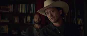 Movie still from “The Mule” (2018), directed by Clint Eastwood – A man in a cowboy hat is looking at the camera while another man sits in the background; Close Up shot, Over the shoulder angle