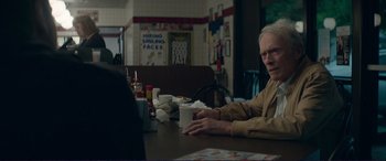 Movie still from “The Mule” (2018), directed by Clint Eastwood – An older man sitting at a table with a cup of coffee; Medium shot, Over the shoulder angle