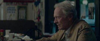Movie still from “The Mule” (2018), directed by Clint Eastwood – An older man sitting at a table in front of a painting; Close Up shot, Over the shoulder angle