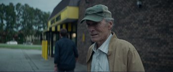 Movie still from “The Mule” (2018), directed by Clint Eastwood – An older man wearing a hat standing on the sidewalk; Close Up shot, Over the shoulder angle