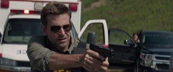 Movie still from “The Mule” (2018), directed by Clint Eastwood – A man holding a gun while standing next to a truck; Medium shot, Over the shoulder angle