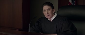 Movie still from “The Mule” (2018), directed by Clint Eastwood – A woman in a judge's robe sitting in front of a microphone; Close Up shot, High angle