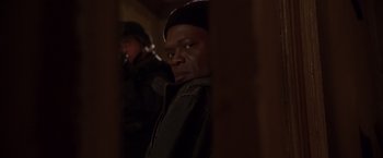 Movie still from “The Negotiator” (1998), directed by F. Gary Gray – A man standing next to another man in a dark room; Close Up shot, Over the shoulder angle