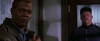 Movie still from “The Negotiator” (1998), directed by F. Gary Gray – A man standing in front of a window holding a cell phone; Close Up shot, Over the shoulder angle