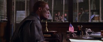 Movie still from “The Negotiator” (1998), directed by F. Gary Gray – A man sitting at a desk in front of an american flag; Medium shot, Over the shoulder angle