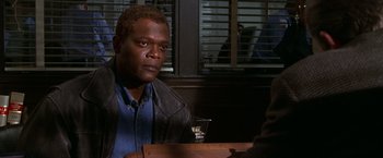 Movie still from “The Negotiator” (1998), directed by F. Gary Gray – A man sitting at a table with a glass of wine in front of him; Medium shot, Over the shoulder angle