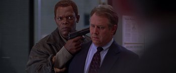 Movie still from “The Negotiator” (1998), directed by F. Gary Gray – A man holding a gun next to another man in a suit and tie; Medium shot, Over the shoulder angle