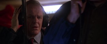 Movie still from “The Negotiator” (1998), directed by F. Gary Gray – An older man wearing a suit and tie while listening to headphones; Close Up shot, Over the shoulder angle