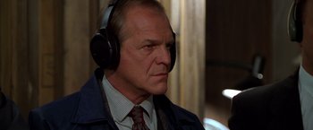 Movie still from “The Negotiator” (1998), directed by F. Gary Gray – An older man wearing headphones while sitting in a room; Close Up shot, Over the shoulder angle
