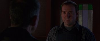 Movie still from “The Negotiator” (1998), directed by F. Gary Gray – A man standing next to another man in a room; Close Up shot, Over the shoulder angle