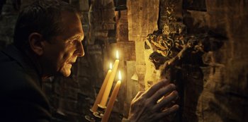 Movie still from “Guillermo del Toro's Cabinet of Curiosities” (2022), directed by Keith Thomas – An old man holding two lit candles in front of a wall; Close Up shot, Over the shoulder angle