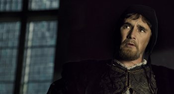 Movie still from “The Other Boleyn Girl” (2008), directed by Justin Chadwick – A man with a beard wearing a black and gold outfit; Close Up shot, Over the shoulder angle