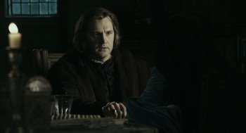 Movie still from “The Other Boleyn Girl” (2008), directed by Justin Chadwick – A man sitting at a table with a glass of water; Medium shot, Over the shoulder angle
