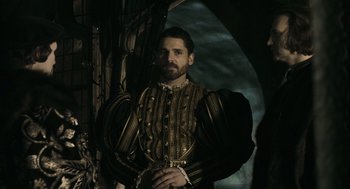 Movie still from “The Other Boleyn Girl” (2008), directed by Justin Chadwick – A man in a black and gold outfit standing in front of a window; Medium shot, Over the shoulder angle